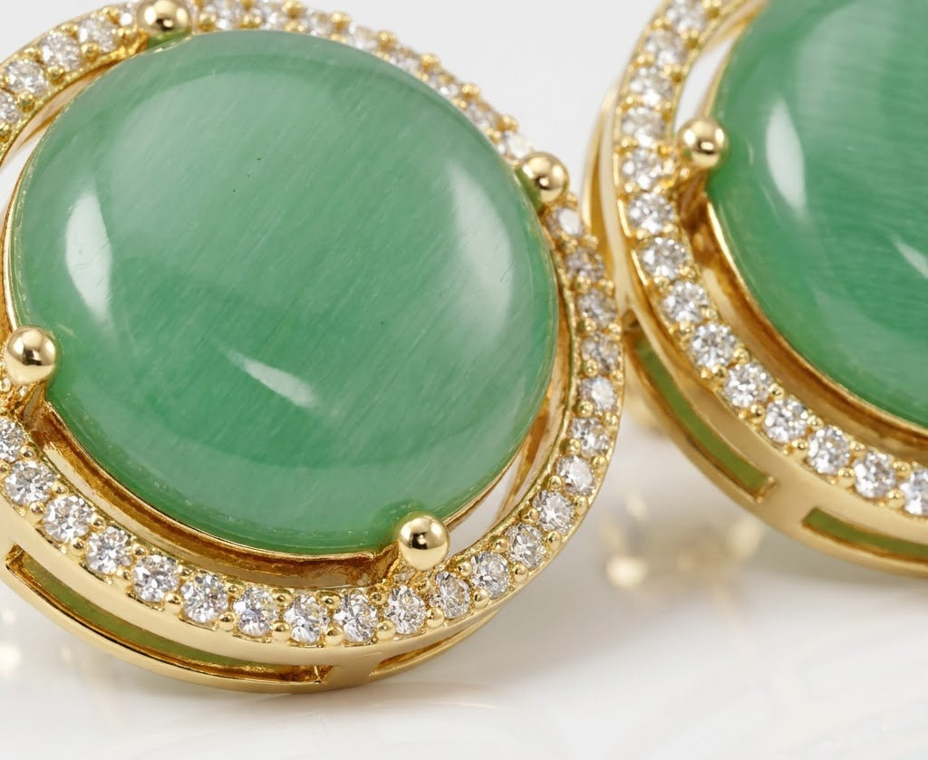 Gold round stud earrings featuring large green cabochon gemstones surrounded by a halo of small clear pavé stones, shown in a close-up studio shot.