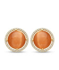 A pair of gold round stud earrings featuring large orange cat's eye cabochons surrounded by a halo of small clear pavé stones, set against a plain white background.