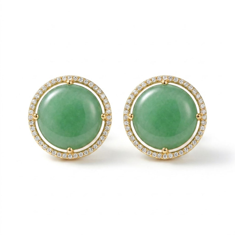 A pair of gold round stud earrings featuring smooth aqua blue cabochon gemstones surrounded by a halo of small clear stones, set against a plain white background.