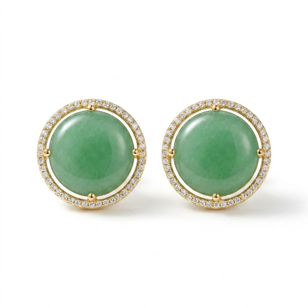 A pair of gold round stud earrings featuring smooth aqua blue cabochon gemstones surrounded by a halo of small clear stones, set against a plain white background.